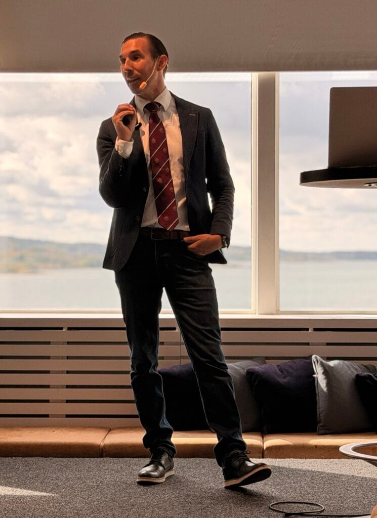 Markus Abrahamsson föreläser om AI, i kavaj med headsetmikrofon och havsutsikt i bakgrunden